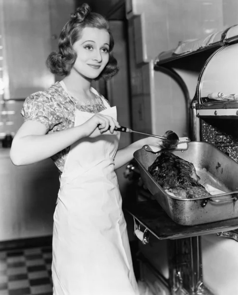 Young woman basting a goose in the kitchen