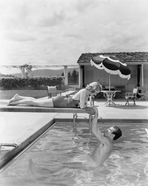 Young woman lying on a diving board with a young man hanging from it
