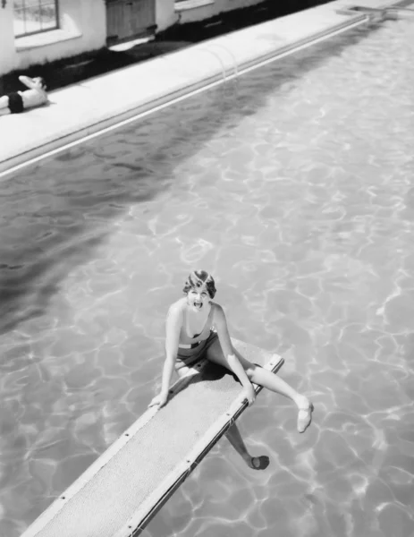 High angle view of a woman sitting on a diving board and looking feared