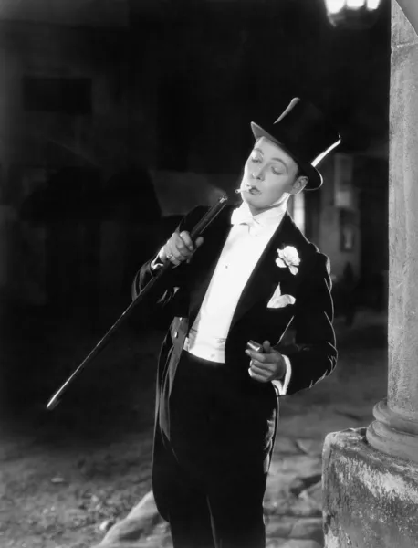 Young man in formal clothing lighting his cigarette with his walking stick