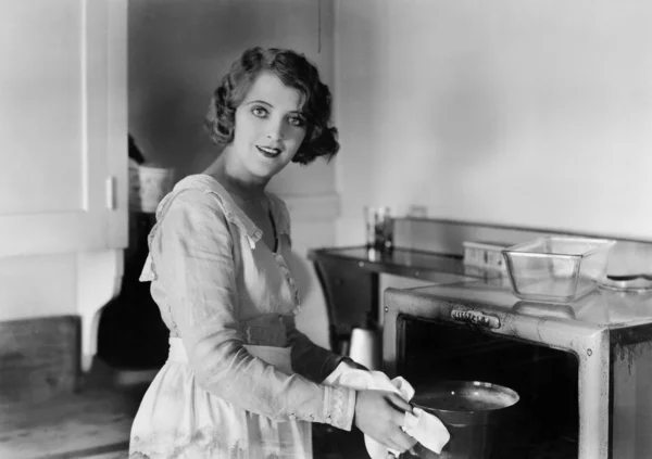Young woman in her kitchen putting a pot into the oven