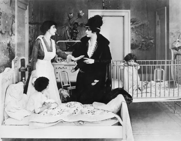 A woman with her nanny and two children in a bedroom talking with each other