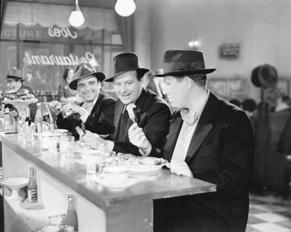 Three men sitting at the counter of a diner