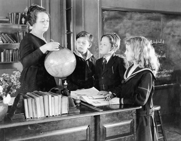 Teacher in a classroom with three pupils pointing to a globe