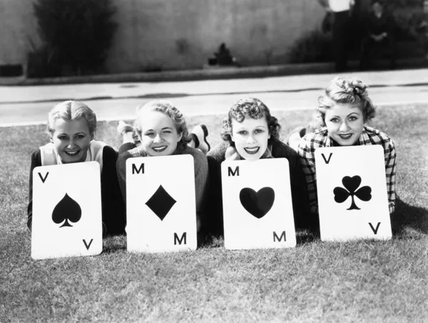 Four women are well suited to lay on the grass with playing cards in front of them