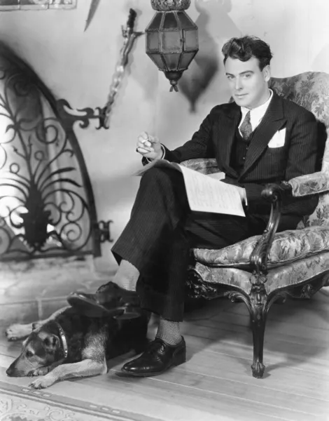 Young man sitting in an armchair next to a fire place with his dog by his feet
