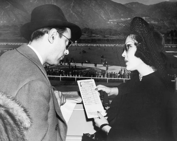 Elegant couple at a horse race looking at a program