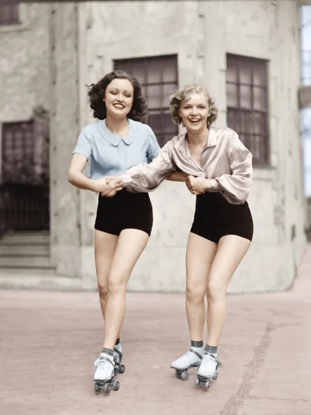 Portrait of two young women with roller blades skating on the road and smiling