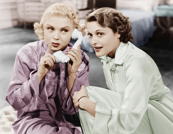 Two women sitting together and listening on the telephone receiver