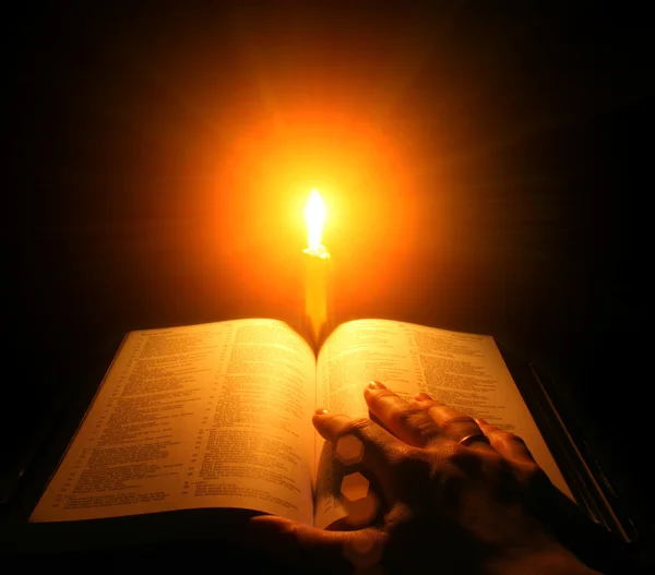 Una bibbia aperta su un tavolo accanto a una candela — Foto Stock