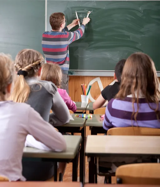 Jonge mannelijke leraar wiskunde op blackboard uitleggen — Stockfoto