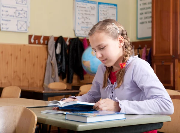 Linda chica leyendo libro en el aula en la escuela — Foto de Stock