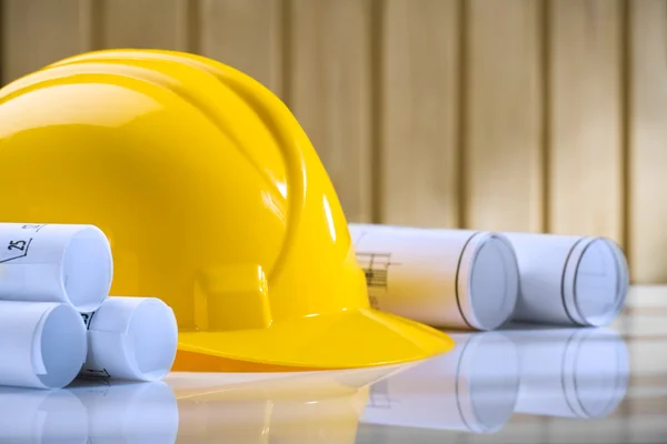 stock image Yellow helmet and rolls of blueprints on table