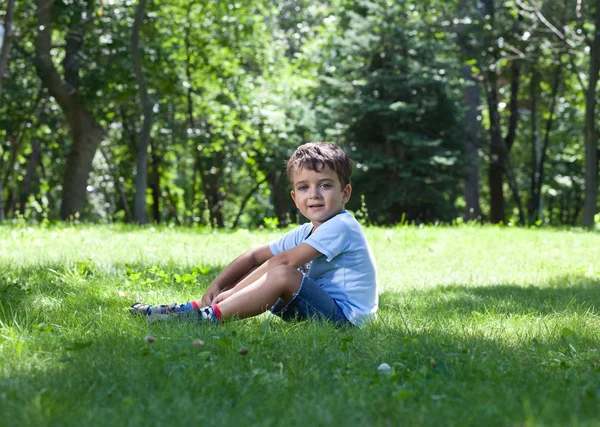 잔디 위에 앉아 있는 귀여운 어린 소년의 사진 — 스톡 사진