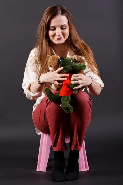 Девушка с мягкими игрушками сидит на стуле — стоковое фото
