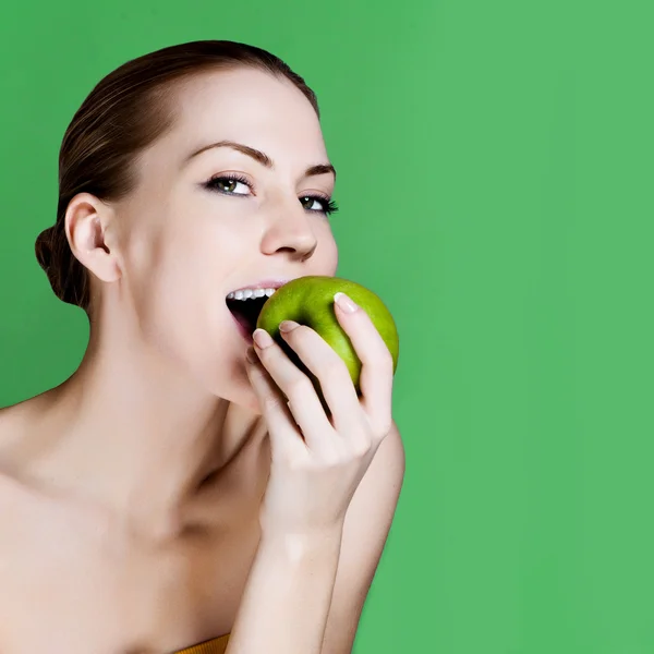 Frau isst Apfel lächelnd auf grünem Hintergrund. Gesunde Ernährung ehrliche Frau. — Stockfoto