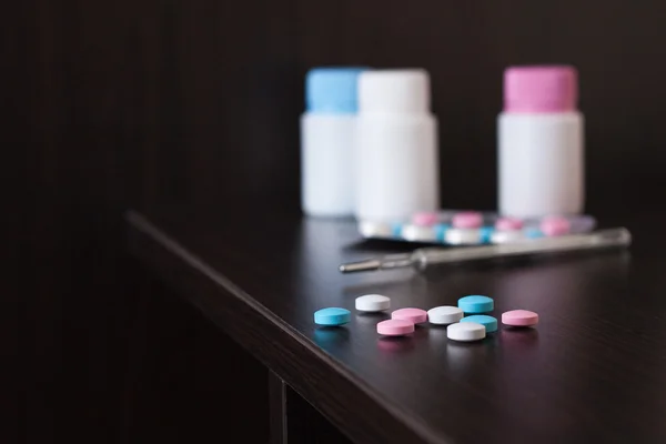 Pílulas coloridas e termômetro na mesa marrom — Fotografia de Stock
