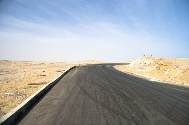 Arka planda bulutlu gökyüzü olan bir çölde asfalt yol