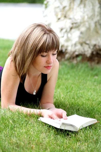 Молода щаслива жінка дивиться на камеру, читаючи книгу — стокове фото