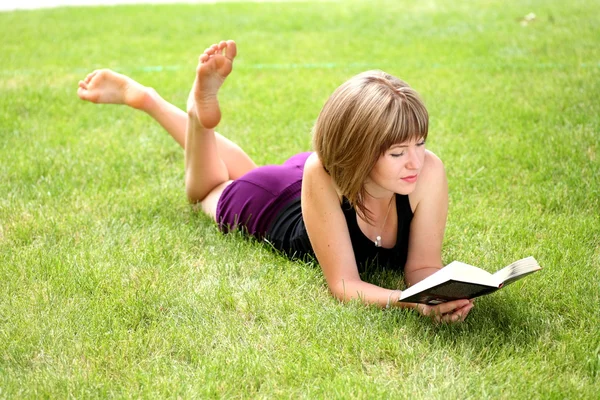 Fiatal, boldog nő néz a kamerába olvasás közben egy könyvet — Stock Fotó