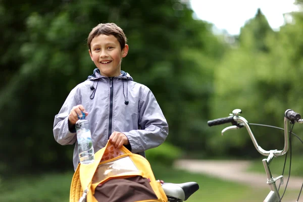 Молодой мальчик с велосипедом с чистой водой расслабляющий на открытом воздухе — стоковое фото