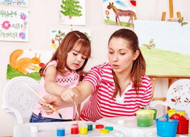 Child with teacher draw paints in play room. clipart