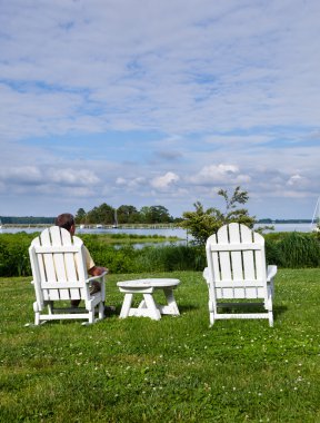 Single senior man in white chairs overlooking bay clipart