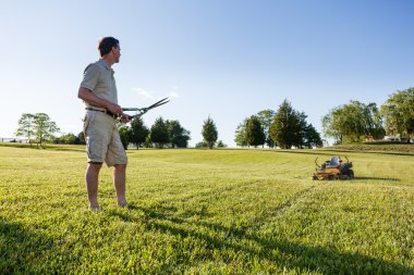 Senior man cutting grass with shears clipart