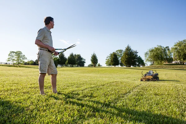 Homem sênior cortando grama com tesouras — Fotografia de Stock