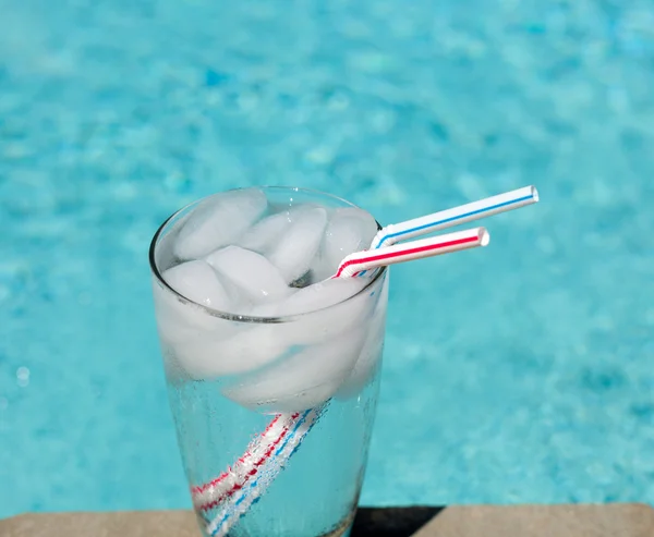 Glas Wasser mit Eiswürfeln auf der Seite des Pools — Stockfoto