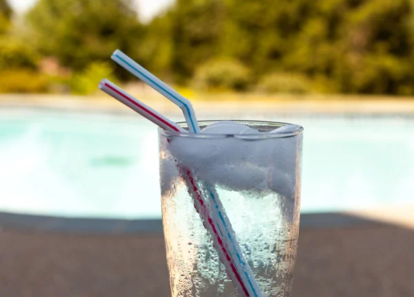 Glas vatten med isbitar på sidan av pool — Stockfoto