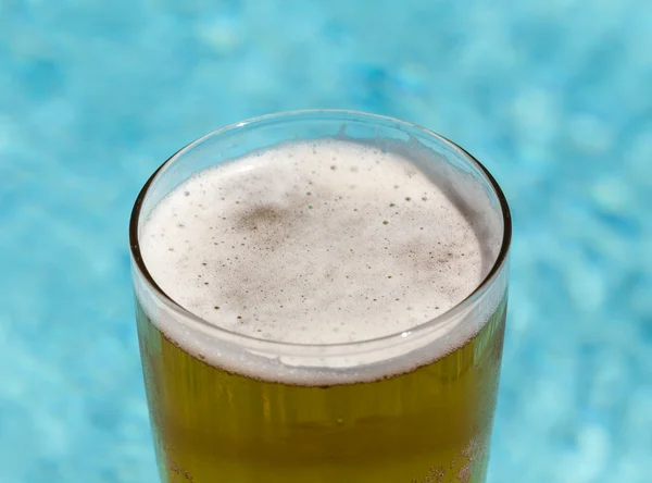 Glass of beer on edge by poolside — Stock Photo, Image