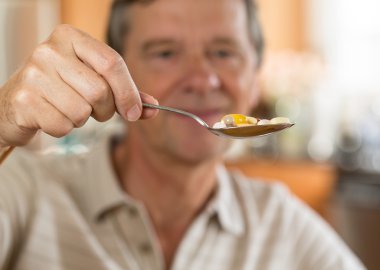 Senior man eating a spoon of vitamins clipart