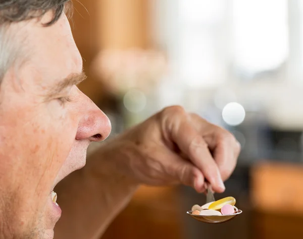 Hombre mayor comiendo una cucharada de vitaminas — Foto de Stock