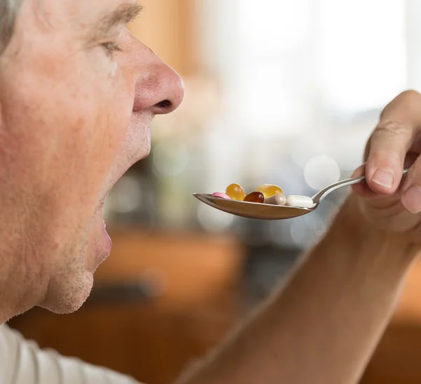 Senior man eating a spoon of vitamins — Stock Photo, Image