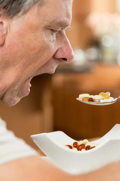 シニア男性のビタミンのスプーンを食べる — ストック写真