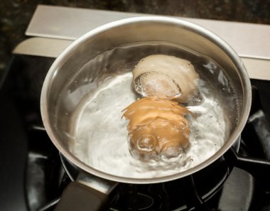 Two boiling eggs in stainless saucepan clipart