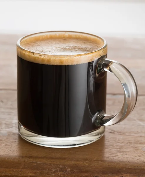Zwarte koffie en schuim in glazen mok houten tafel — Stockfoto