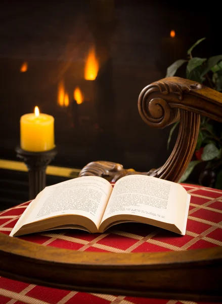 Brožovaná kniha otevřené na židli u ohně a svíčka — Stock fotografie