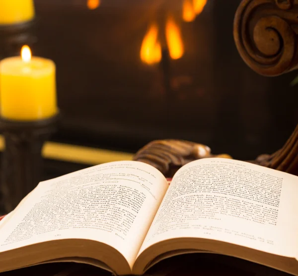 Бумажная книга, открытая на стуле при свете огня и свечи — стоковое фото