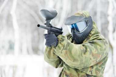 Paintball player with marker at winter outdoors clipart