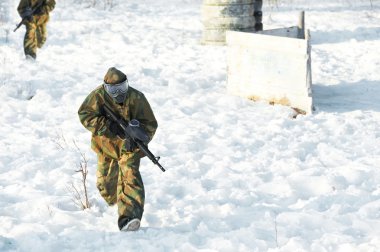 Paintball player with marker at winter outdoors clipart