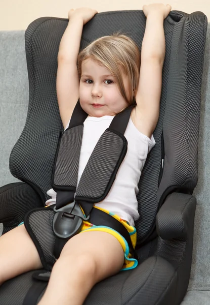 Menina pequena sentada em um assento de segurança do carro com cinto de segurança — Fotografia de Stock