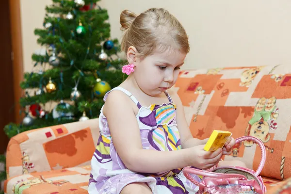 Pequeña chica sonriente sentada en el sofá detrás del árbol de Navidad —  Fotos de Stock