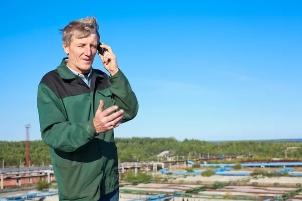 Mature man in working clothes speaking on cellphone outdoor — Stock Photo, Image
