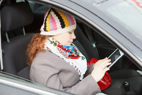 Arabanın yolcu koltuğunda oturan ve elektronik cihaz tutan genç bir beyaz kadın — Stok fotoğraf