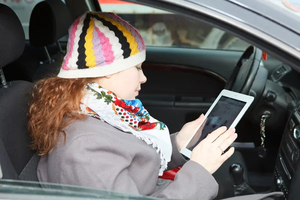 Joven mujer caucásica sentada en el coche en el asiento del pasajero y sosteniendo el dispositivo electrónico —  Fotos de Stock