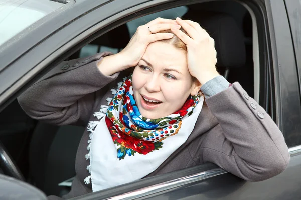 Pretty young expression Caucasian woman holding head by hands sitting in car — Stock Photo, Image