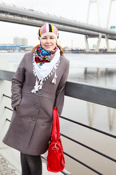Portret van gelukkige jonge Kaukasische teef met rode zak staande op embankment — Stockfoto