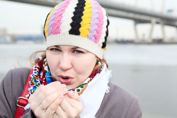 Portrait of frozen young Caucasian female warming hands and standing on embankment. Close up. Bridge on background — Stock Photo, Image